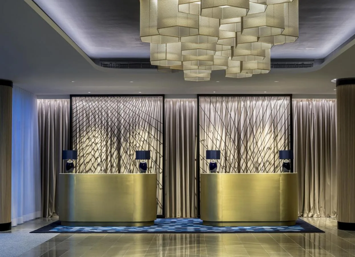 a lobby with a row of gold elevators and a chandelier at The Lowry Hotel Manchester in Manchester